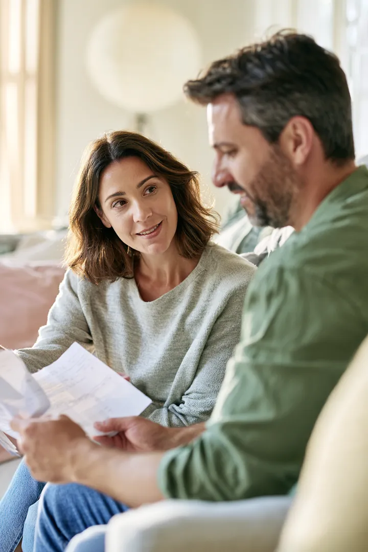 Couple on a sofa calmly reviewing household bills together while weighing an amone loan against a card